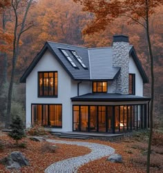 a house in the woods with lots of leaves on the ground and trees around it