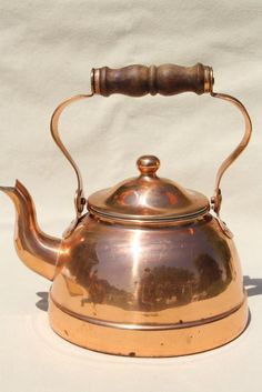 an antique copper tea kettle with a wooden handle on a white tableclothed background