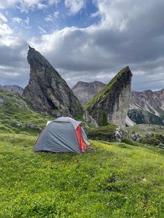 a tent pitched up in the grass with mountains in the back ground and cloudy skies overhead