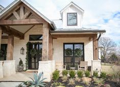 a white house with two wooden chairs on the front porch and plants in pots outside