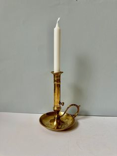 a brass candle holder with a single white candle on it's side and a hook in the middle