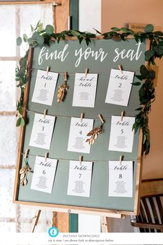 a seating chart is displayed on a easel with clothes pins and greenery around it