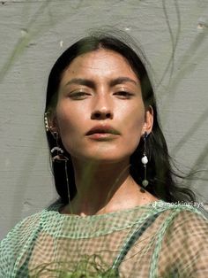 a woman with long black hair wearing green and white checkered shirt, earrings and necklace