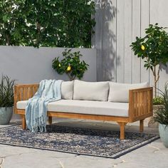 a wooden couch sitting on top of a blue rug next to potted plants and trees