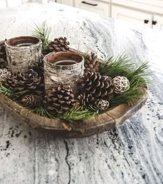 some pine cones are sitting on a wooden plate with two glasses and evergreen needles in the center