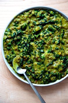 a white bowl filled with spinach and other food on top of a wooden table