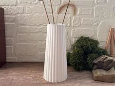 a white vase sitting on top of a wooden table next to a rock and plant