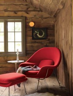 a red chair and footstool in a room with wood paneling on the walls