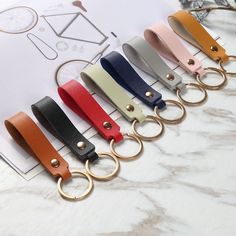 six different colors of leather keychains with gold rings on each side and one black, white, red, blue, yellow, pink, green