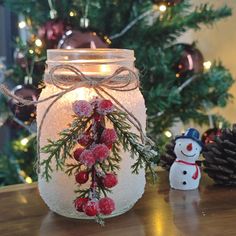 a jar filled with snow and berries next to a christmas tree