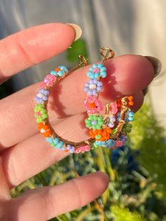 Handmade beaded hoop earrings 3.5 cm in diameter. The daisies are blue, pink, purple, green, and orange; perfect for spring or summer. They are lightweight, and the beads are mounted on a gold colored stainless steel hoop with a latch back closure. Spring Beaded Flower Earrings For The Beach, Spring Beach Flower Beaded Earrings, Handmade Hoop Earrings For Spring, Spring Trendy Dangle Hoop Earrings, Trendy Spring Dangle Hoop Earrings, Trendy Dangle Hoop Earrings For Spring, Spring Rainbow Earrings, Multicolor Beaded Flower Earrings For Spring, Summer Hoop Earrings With Tiny Beads