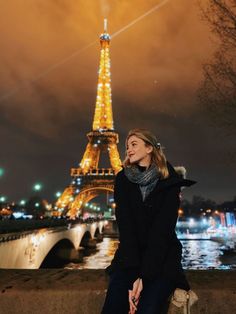 a woman sitting in front of the eiffel tower at night