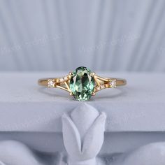 a ring with an oval green stone surrounded by small white diamonds on a white cloth