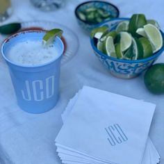 a table topped with blue cups filled with liquid and limes next to paper napkins