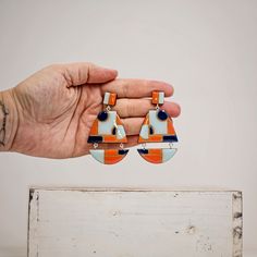 "Large, but light and very elegant statement earrings. Made with wooden elements and finished with epoxy resin. These geometric earrings come in two variations - hypoallergenic silicone studs and metal clip on. You have to choose from variations the type you prefer. The earrings have bright geometric pattern in blue and orange and can be perfect addition to your jewelry collection.  These cool, trendy earrings definitely will brighten your autumn wardrobe. The length of the earrings is 7.0 cm. The clip ons does not contain nickel. Please keep in mind that colors may vary slightly from those viewed on your monitor. Please see \"Shop Policies\" section for more important information about shipping, refunds, custom options and more. CARE INSTRUCTIONS - store in a clean, dry place. Use of oils Modern Orange Drop Earrings, Modern Blue Geometric Earrings, Bold Orange Drop Earrings, Homemade Earrings, Autumn Wardrobe, Colorful Earrings, Trendy Earrings, Blue And Orange, Geometric Earrings