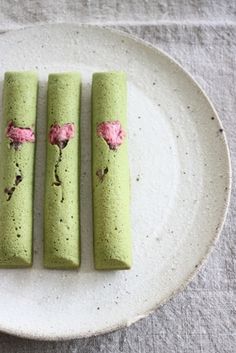 three green crepe sticks with pink flowers on them sitting on a white plate