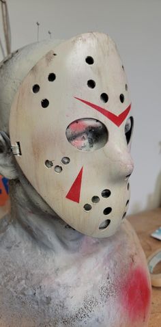 a white mask with red and black markings on it sitting on top of a wooden table