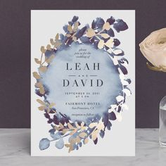 a blue and gold wedding card on a table next to a vase with flowers in it