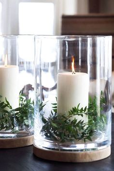 two clear glass vases with candles and greenery in them sitting on a table