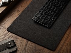 a black keyboard sitting on top of a wooden table next to a wallet and watch