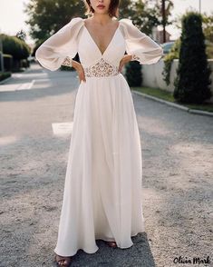 a woman standing in the middle of a road wearing a white dress with sheer sleeves