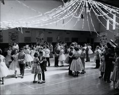 an old black and white photo of children dancing in a dance hall with streamers overhead