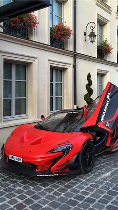 a red and black sports car parked in front of a tall building with flowers on the windows