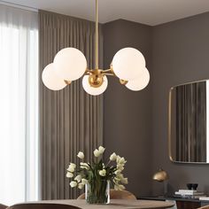 a dining room table with flowers in a vase on it and two lights hanging from the ceiling