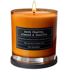 an orange candle with a black label on the front and bottom, sitting in a glass holder