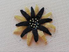 a black and gold flower brooch with beads on the center, sitting on a white surface