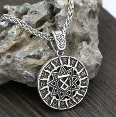 a silver pendant with an intricate design on it's side sitting next to some rocks