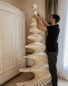 a man is decorating a christmas tree made out of folded book pages and plywood