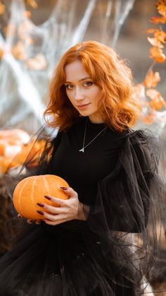 a woman with red hair holding a pumpkin in her hands and wearing a black dress