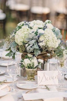 there is a vase with white flowers on the table and place cards in front of it