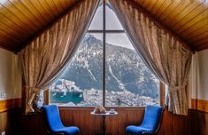 two blue chairs sitting in front of a window with mountains out the window behind them