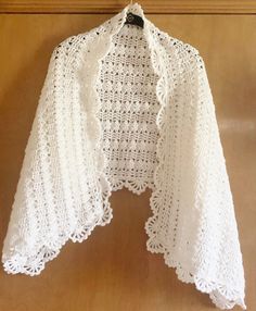 a white crocheted shawl hanging on a wooden door frame with a black hanger