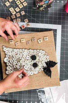 two hands are making buttons on a piece of burlock with letters and numbers