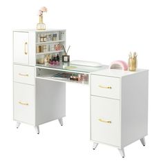 a white desk with gold handles and drawers on it's sides, next to a pink flower