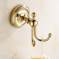 a gold colored wall mounted faucet on the side of a white wall with a crocheted basket underneath it