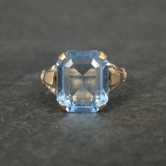 This gorgeous vintage ring is 10K Gold Filled. It features a stunning 10x12mm faceted blue glass stone. The face of this ring measures 1/2 of an inch north to south with a rise of 7mm off the finger. Size: 9 Marks: 1/20 10K GF, MH Condition: Old new stock - excellent Vintage Blue Diamond Cut Jewelry, Vintage Blue Jewelry With Diamond Cut, Blue Vintage Jewelry With Diamond Cut, Vintage Blue Gemstone Birthstone Ring, Vintage 14k Gold Blue Jewelry, Vintage Blue 14k Gold Jewelry, Blue Gemstone Vintage Jewelry, Vintage Blue Topaz Ring In 14k Gold, Vintage Topaz Birthstone Promise Ring