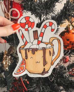 a hand holding up a christmas ornament with candy canes on it and a mug