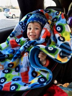 a little boy sitting in the back seat of a car with a blanket over his head