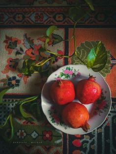 three pomegranates in a white bowl on a floral tablecloth with leaves