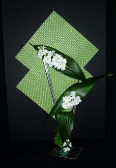 a green vase with white flowers in it on a black tableclothed surface next to a wall