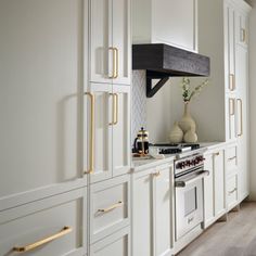 a kitchen with white cabinets and gold trim on the doors, stove top oven and range hood