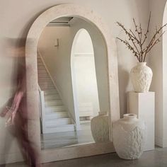 a large white vase sitting on top of a table next to a mirror and stairs