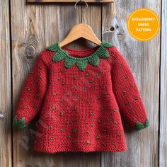 a red sweater with green trim hanging on a wooden wall next to a sign that says strawberry dress pattern