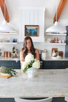 a woman sitting at a kitchen counter in front of a vase filled with white flowers