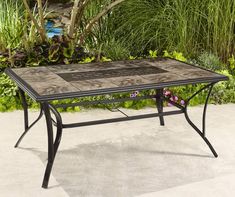 an outdoor table with tile top and metal frame, in front of some flowers on the ground