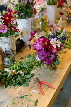 several vases filled with different types of flowers on a wooden table next to scissors